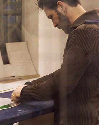 Artisan leaning over a large work table to cut materials in a workshop