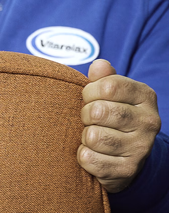 Hand gripping a brown upholstered cushion with a Vitarelax logo in the background