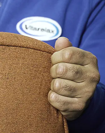 Hand gripping a brown upholstered cushion with a Vitarelax logo in the background